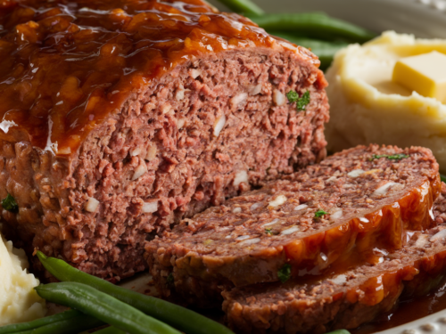 easy meatloaf recipe: A sliced, freshly baked meatloaf topped with tangy glaze, served with mashed potatoes and green beans.