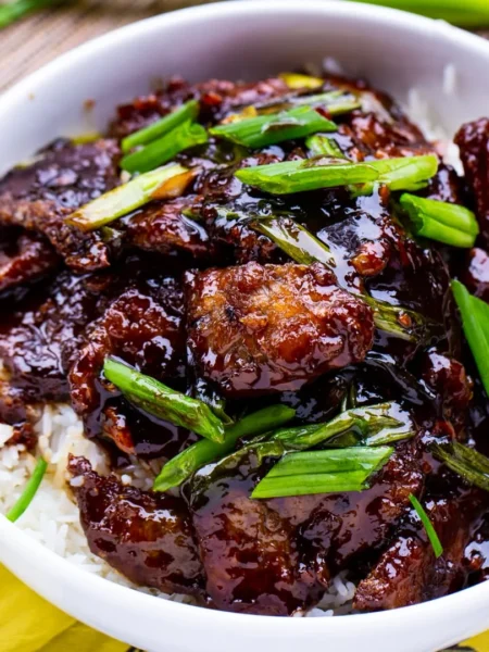 mongolian beef recipe: A delicious plate of Mongolian beef with tender beef slices in a glossy sweet-savory sauce, served over rice and garnished with green onions and sesame seeds.