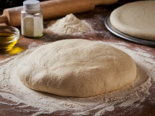 Freshly prepared pizza dough on a floured surface with ingredients around it.
